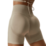 Woman in beige high-waisted workout shorts with mesh panels, highlighting curves and confidence.