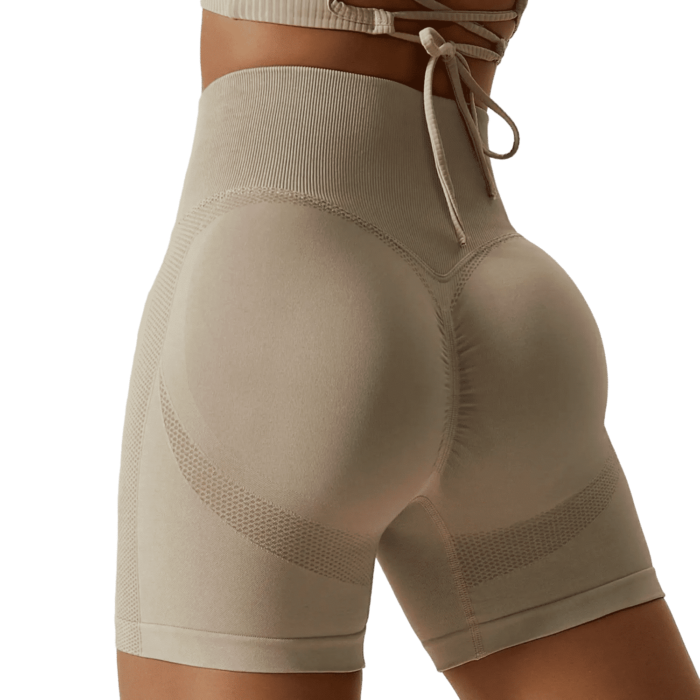 Woman in beige high-waisted workout shorts with mesh panels, highlighting curves and confidence.